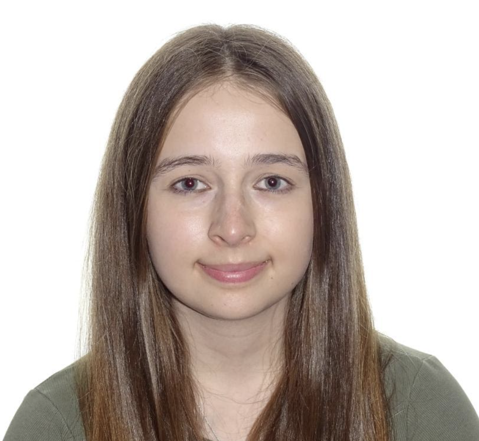 Elena, a young white woman with dark brown hair, looks at the camera from a white background.