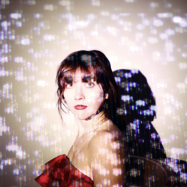 Francesca's head and shoulders looking left at us, wearing a red dress, and dappled with disco lighting